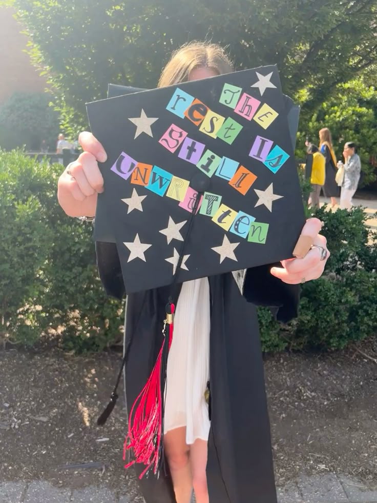 Black graduation cap with silver star cutouts and colourful mixed font stickers spelling out the rest is still unwritten.