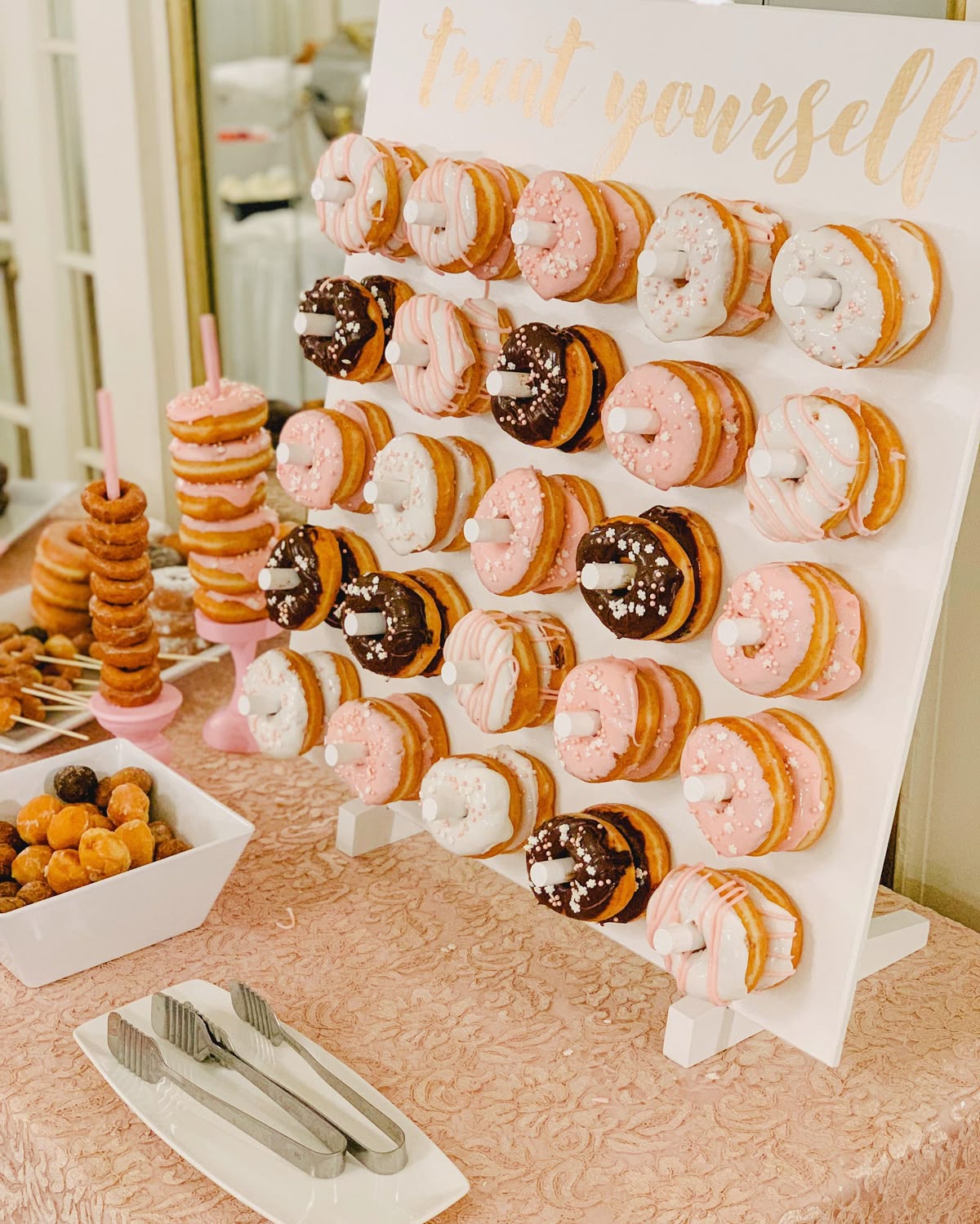 White donut wall display with pink chocolate and glazed donuts at a graduation party dessert table with a treat yourself sign