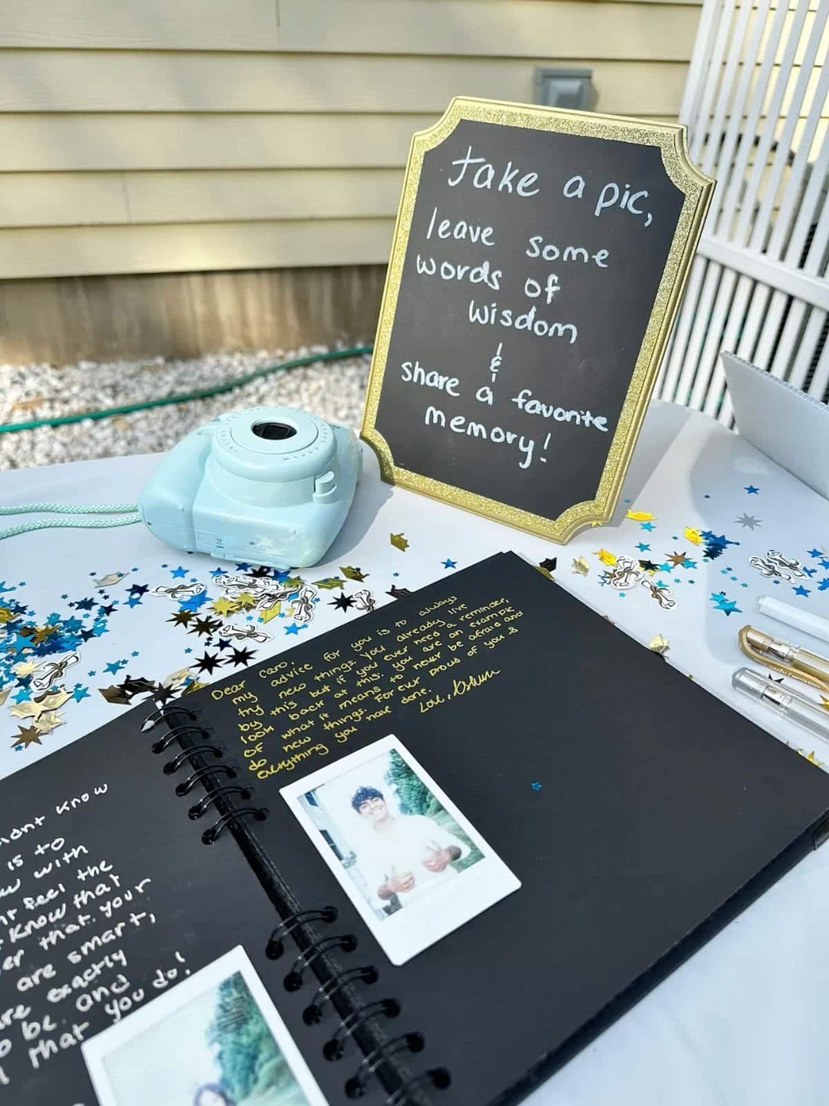 Instax camera and black guestbook on a table at a graduation party with a sign asking guests to take a pic and leave words of wisdom