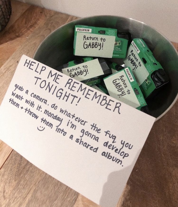 Bowl of Fujifilm disposable cameras with a handwritten sign asking guests to help capture memories at a graduation party