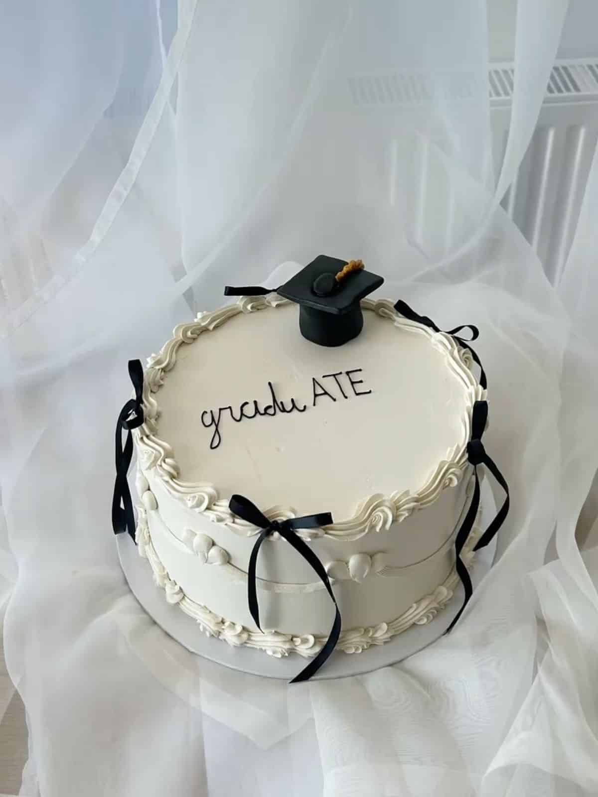 White vintage buttercream graduation cake with ornate piped detailing black ribbon bows and a black graduation cap topper