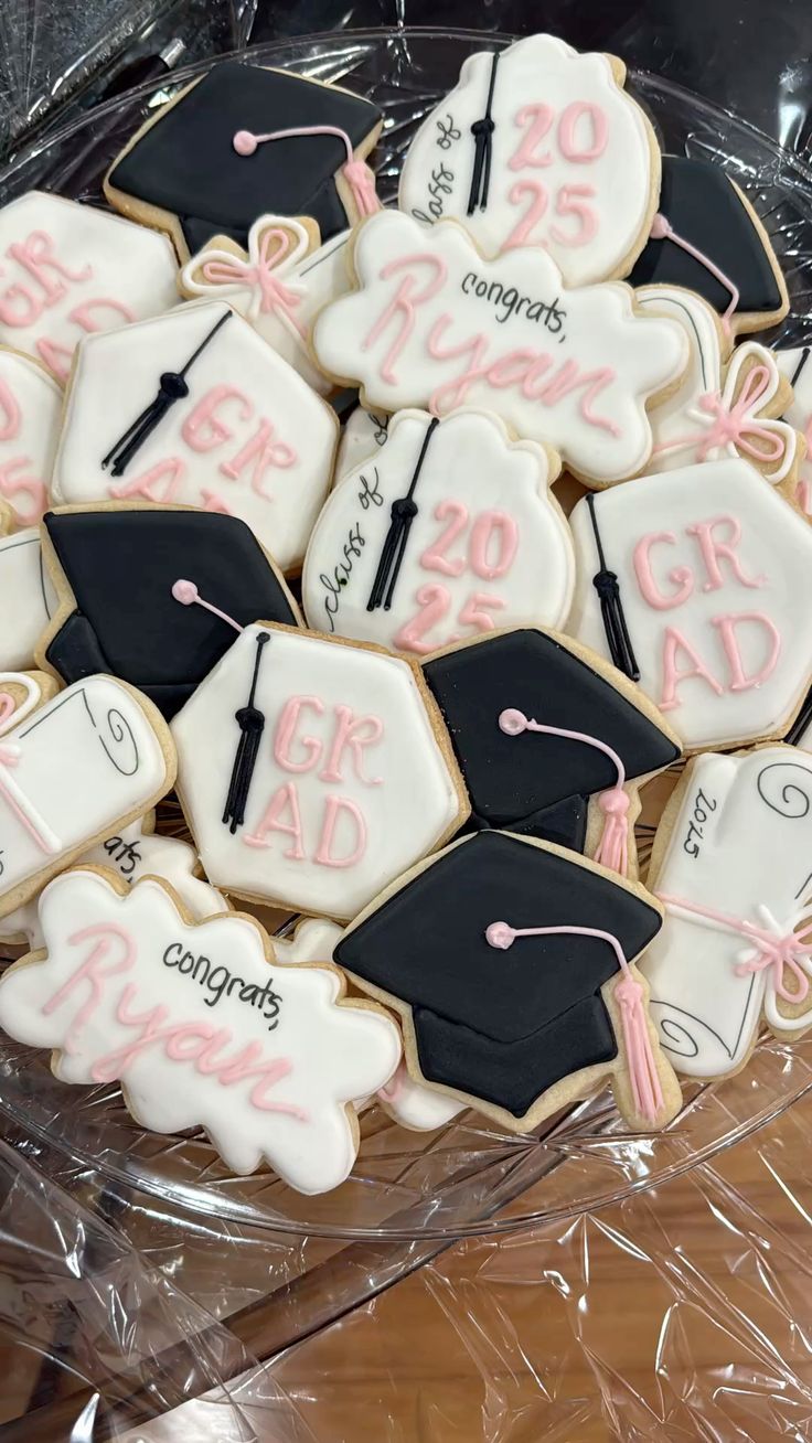 Platter of custom royal iced graduation cookies in black and white with pink details including graduation caps diplomas and the grad's name