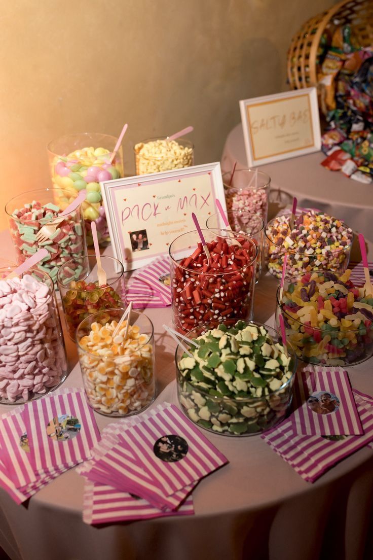 Graduation party lolly bar with glass jars filled with assorted colourful sweets and pick and mix bags on a round table