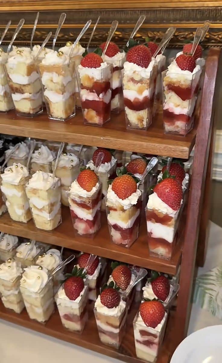 Tiered wooden display stand filled with individual strawberry shortcake dessert cups topped with whipped cream and fresh strawberries at a graduation party