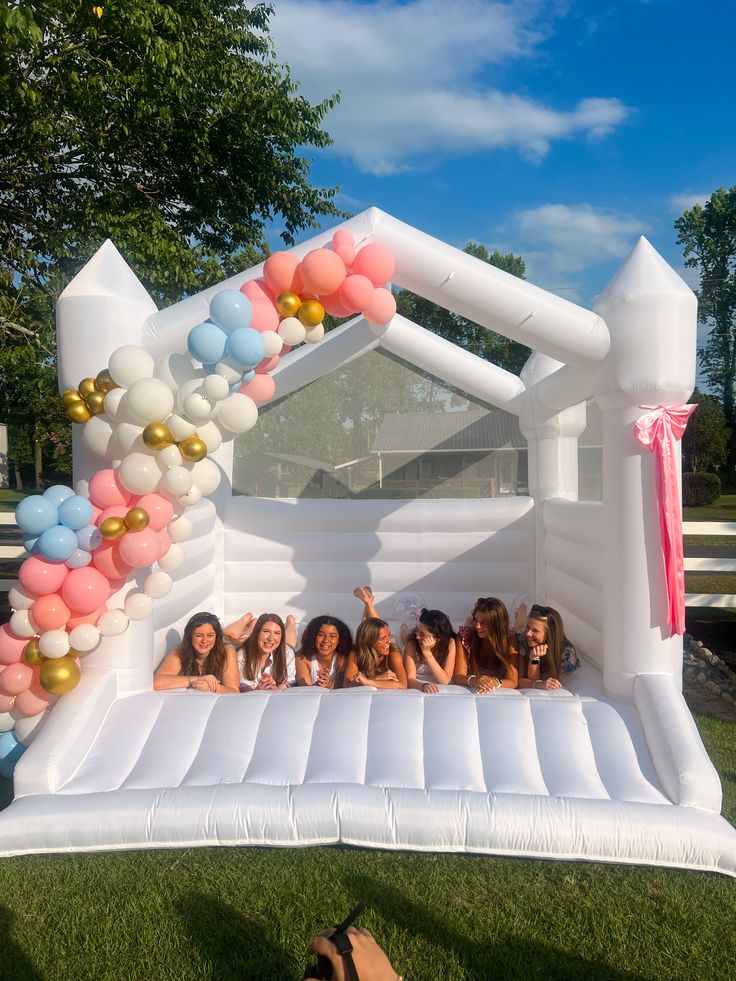 Group of girls laughing inside a white bounce castle decorated with a pastel balloon garland at a graduation party