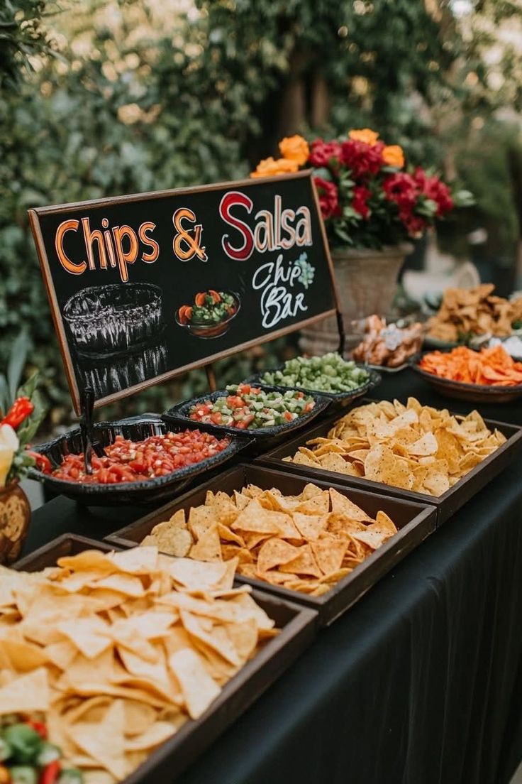 Outdoor graduation party chips and salsa bar with a chalkboard sign multiple salsa options and baskets of tortilla chips on a dark tablecloth