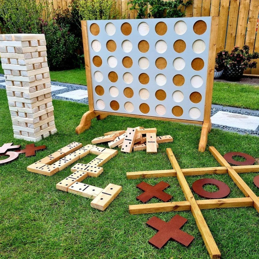 Giant wooden lawn games including Jenga Connect Four dominoes and noughts and crosses set up on grass for an outdoor graduation party