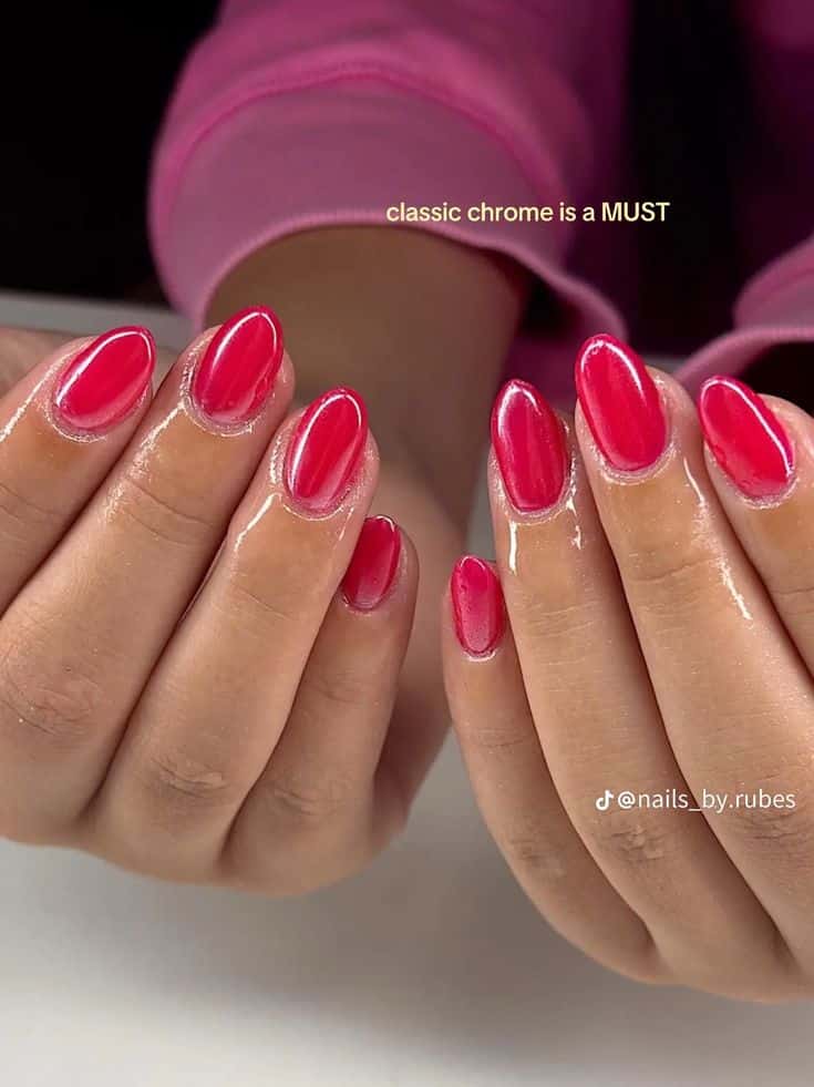 Medium almond nails with a glossy hot pink chrome reflective finish on two hands clasped together, wearing a hot pink sleeve