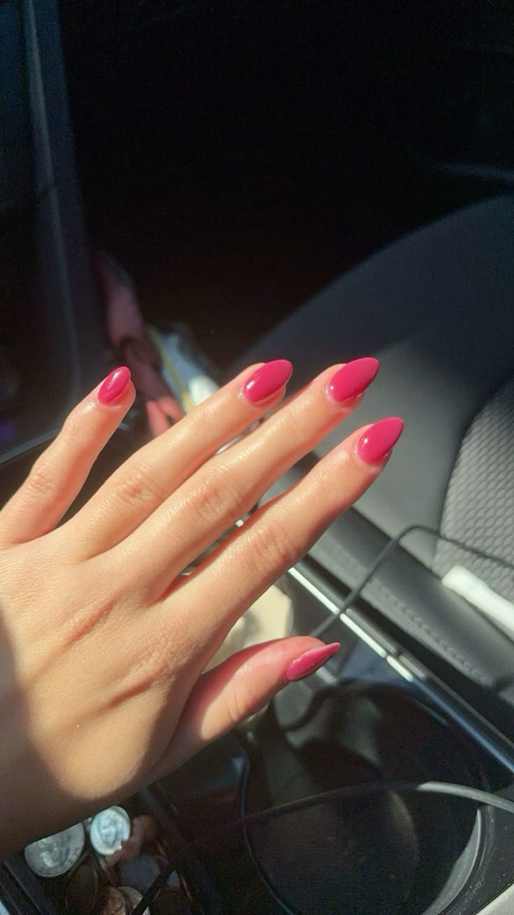 Long almond-shaped nails in a vivid glossy hot pink gel on a hand reaching toward a car interior