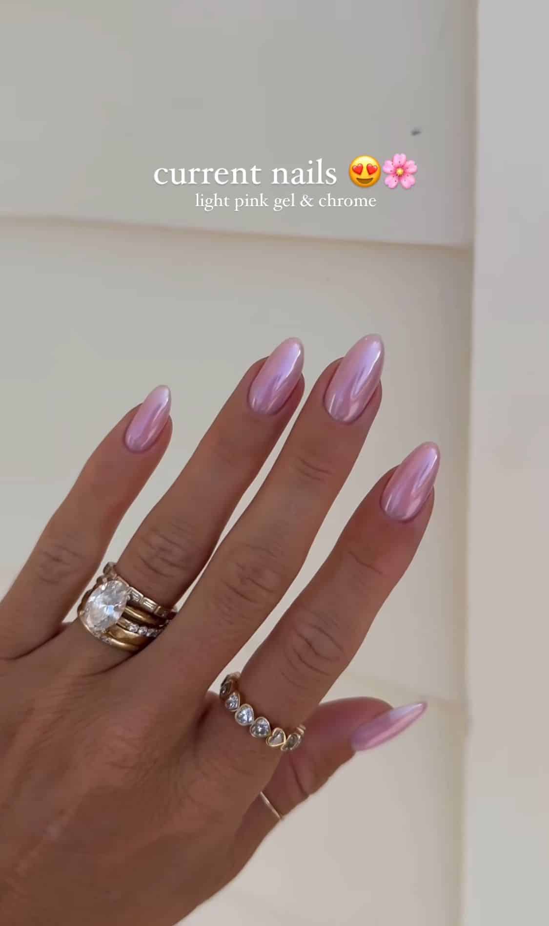 Long almond nails with a light pink gel and iridescent chrome finish on a hand wearing a diamond ring stack and a heart diamond ring