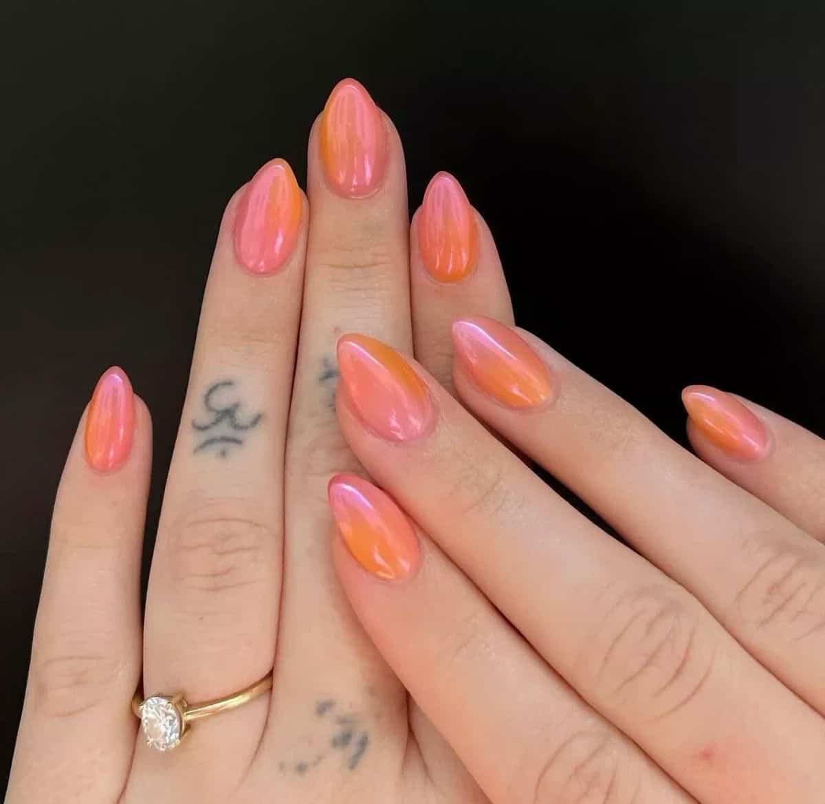 Medium almond nails with a two-tone chrome finish shifting between coral pink and orange, on two hands with a gold solitaire ring