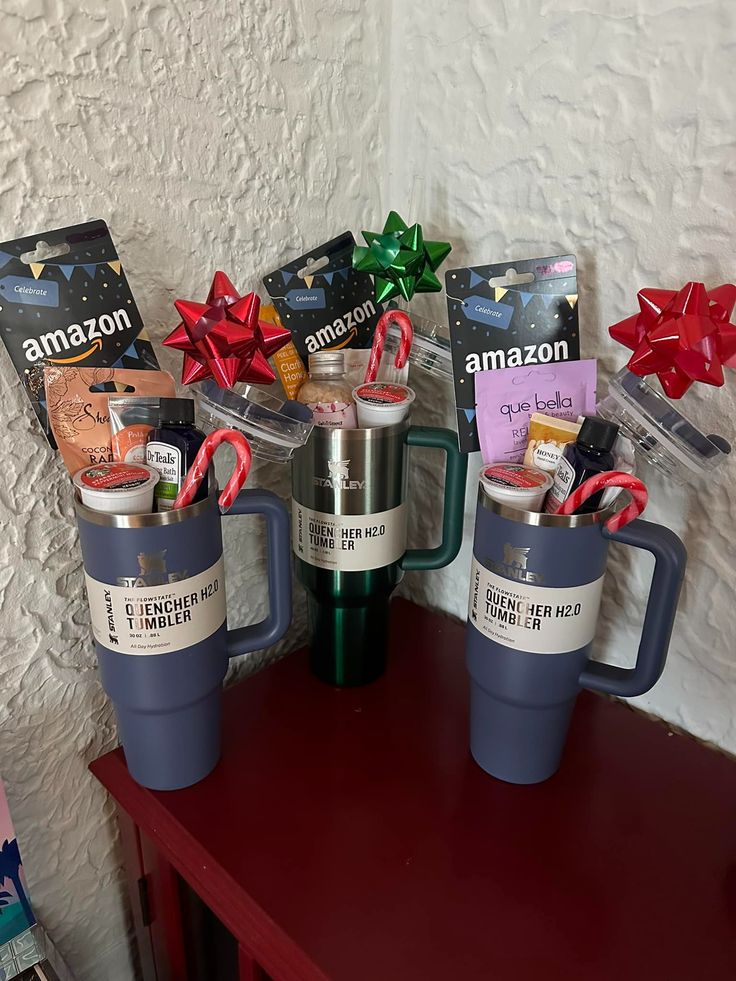 Three Stanley Quencher tumblers in navy and green arranged together with Amazon gift cards, bath products, coffee pods, and candy cane holiday decorations