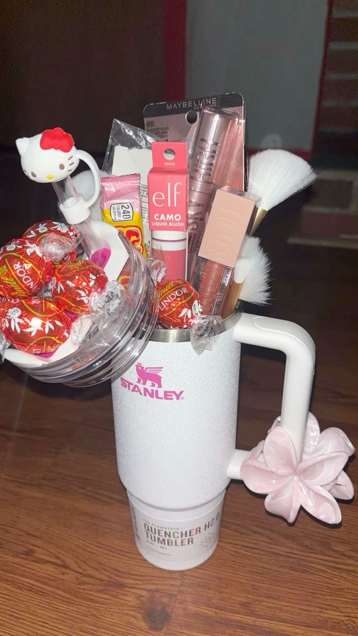 White textured Stanley tumbler filled with Lindt Lindor chocolates, e.l.f. Camo liquid blush, Maybelline mascara, a makeup brush, and a Hello Kitty straw topper