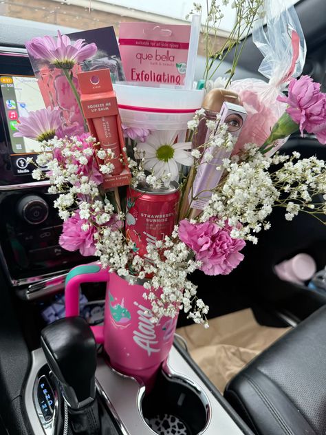 Pink printed Stanley tumbler in a car cup holder filled with pink and white daisies, carnations, baby's breath, Que Bella exfoliating mask, and a strawberry body spray