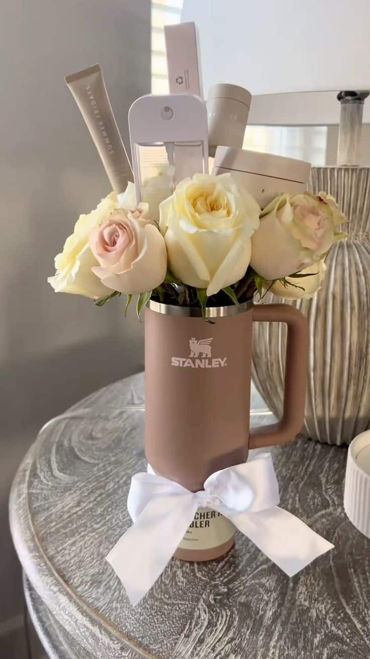 Taupe Stanley tumbler with white ribbon bow filled with cream roses and skincare product tubes from Summer Fridays