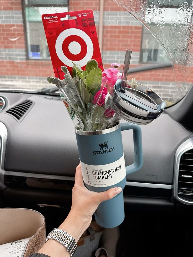 Slate blue Stanley Quencher H2.0 tumbler held in a car with pink flowers, green foliage, and a Target gift card tucked inside