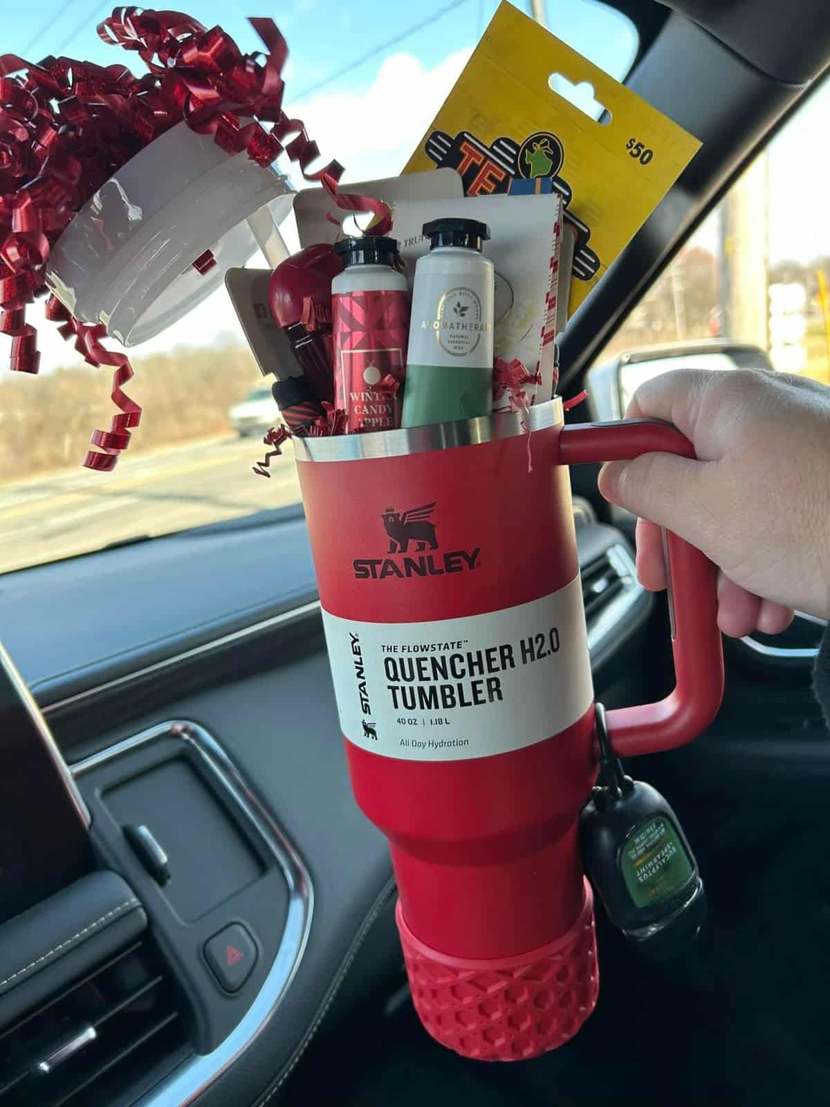 Red Stanley Quencher H2.0 Tumbler filled with Bath and Body Works lotion, aromatherapy products, a $50 gift card, and red curly ribbon