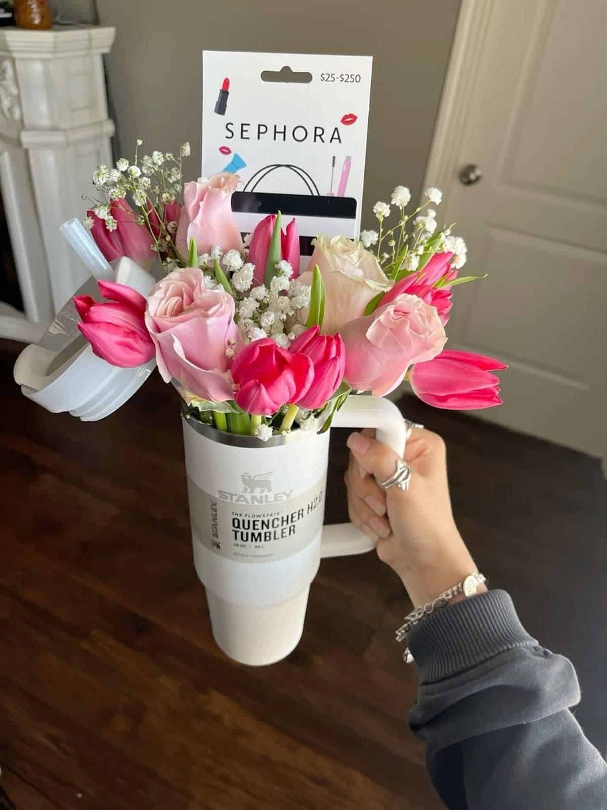 White Stanley Quencher tumbler held by hand and filled with pink tulips, roses, baby's breath, and a Sephora gift card