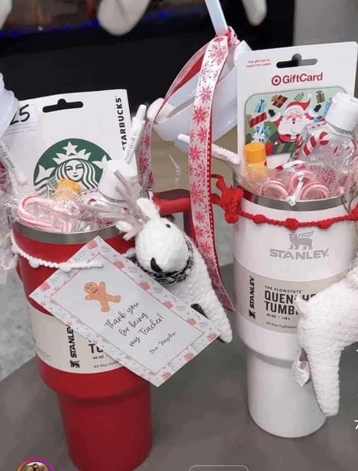 Two Stanley tumblers decorated for Christmas with candy canes, ribbon, a Starbucks gift card, a Target gift card, and a handwritten thank you teacher tag