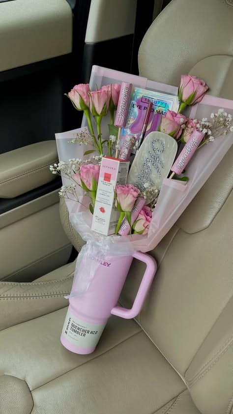 Pink Stanley tumbler wrapped in sheer pink cellophane and filled with pink spray roses, baby's breath, Sephora beauty products, an eye mask, and a rhinestone nail file