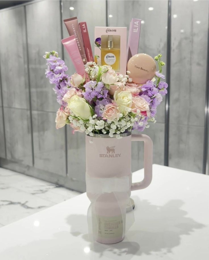 Blush pink Stanley tumbler on marble surface filled with garden roses, sweet peas, baby's breath, and luxury beauty brands including ILIA, Summer Fridays, and Gisou