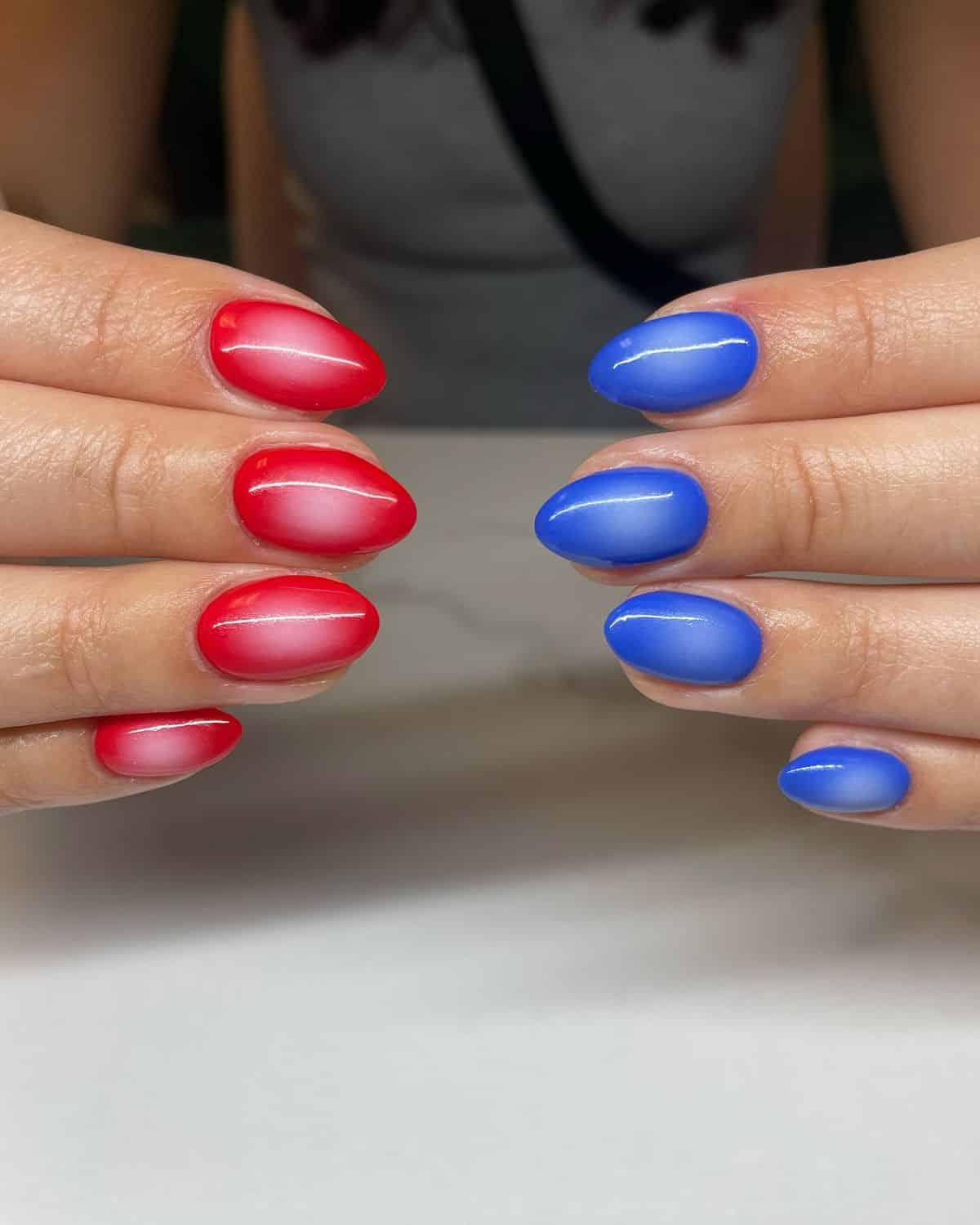 Medium almond nails split between two hands, one hand with aura-finish red nails and the other with aura-finish cobalt blue nails, both showing a soft glowing centre effect.