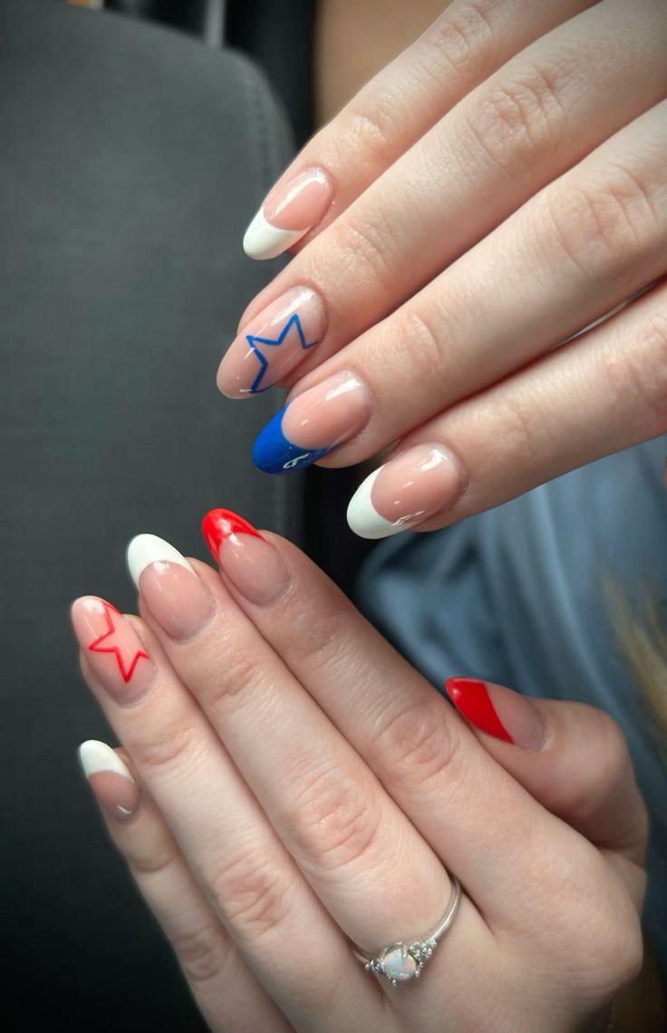 Medium almond nails with a sheer nude base featuring alternating French tips in red and cobalt blue, with small outlined star details on the nail beds, shown on two hands.