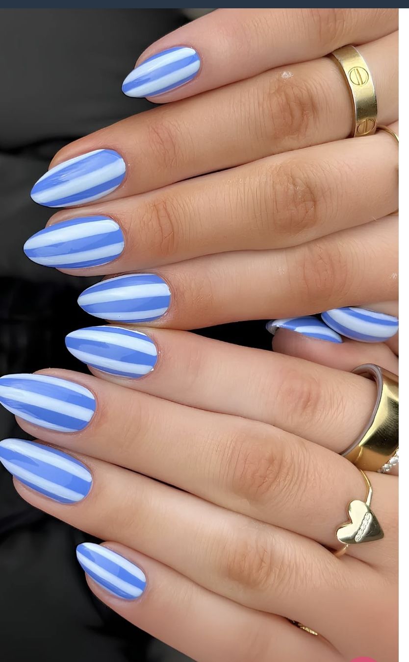 Long almond nails covered in diagonal candy stripes in soft sky blue and white across all fingers on both hands, photographed with gold rings.