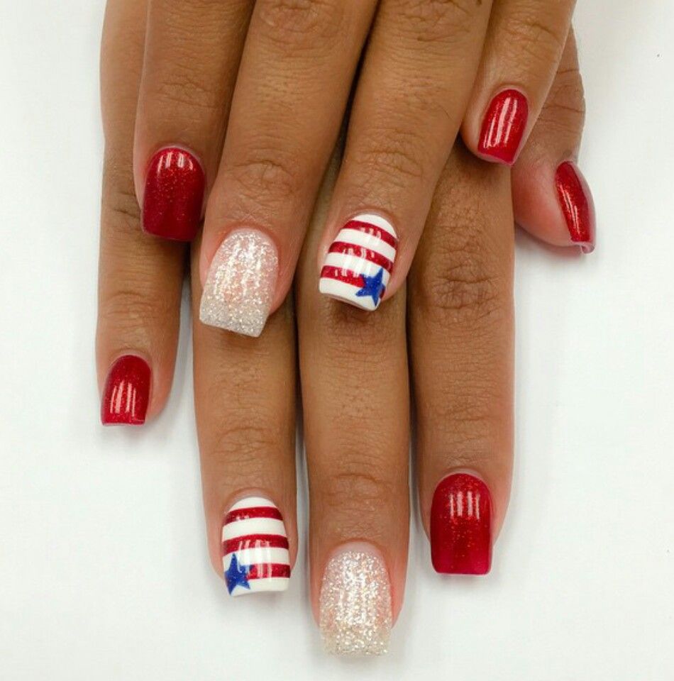 Short square nails with deep red glitter polish on most fingers, one silver glitter nail, and two white accent nails featuring red stripes and a blue star.