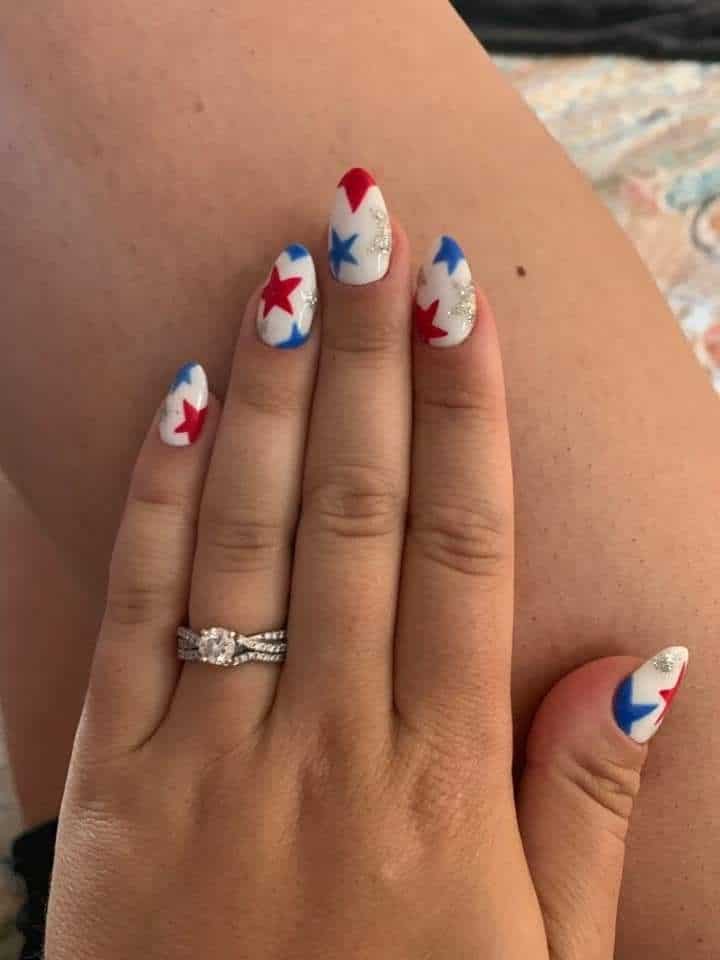 Medium almond nails on a white base covered in scattered red, blue, and silver glitter stars across all fingers, photographed close up.