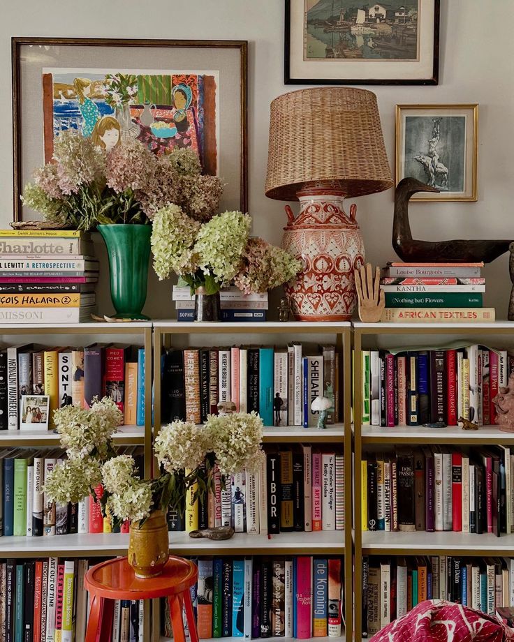 Overflowing bookshelves packed with colourful books, framed artwork, fresh hydrangeas, and eclectic objects