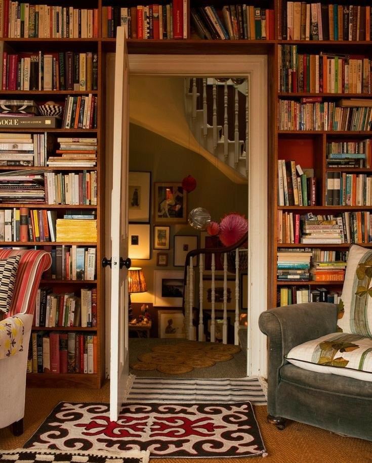 Floor-to-ceiling dark wood built-in bookshelves surrounding a doorway, packed with books, with two armchairs in front