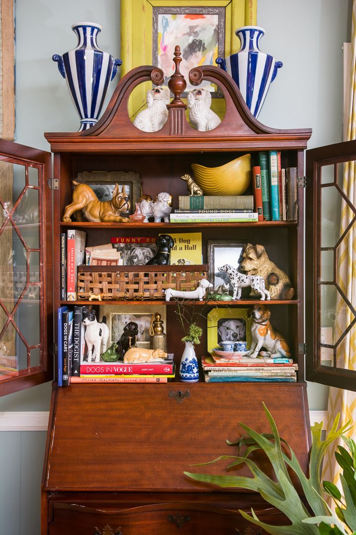 Open antique mahogany secretary cabinet with lattice glass doors displaying a collection of ceramic and figurine dogs alongside dog-themed books, topped with Staffordshire dog figurines and striped blue and white vases.
