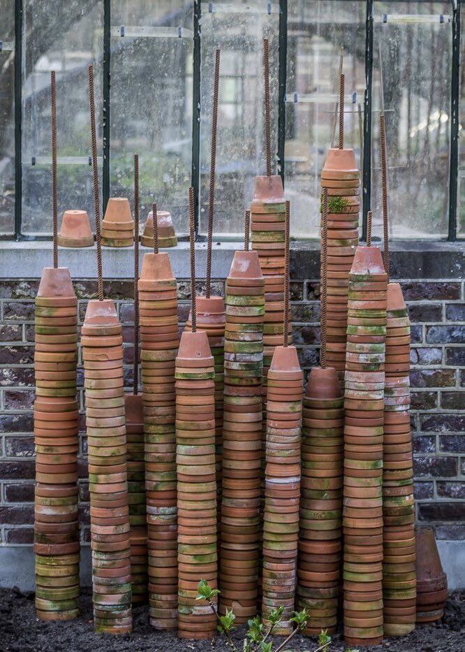 Terracotta pot towers stacked on rebar stakes against a greenhouse wall