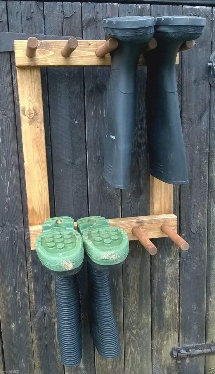 Wood peg rack mounted on a fence holding garden boots