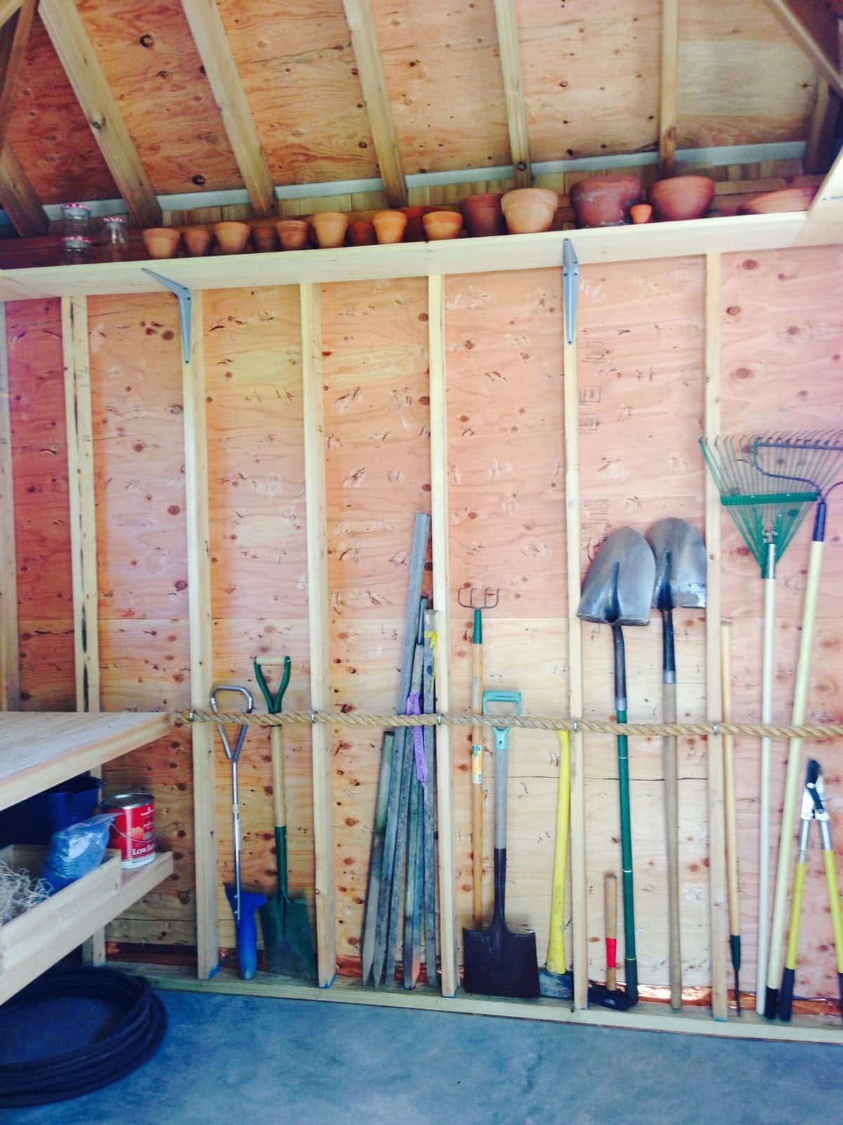 Rope rail strung across a shed wall holding long handled tools