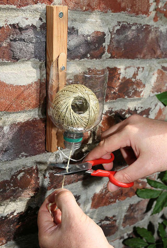 Plastic bottle mounted to a board holding a ball of garden twine