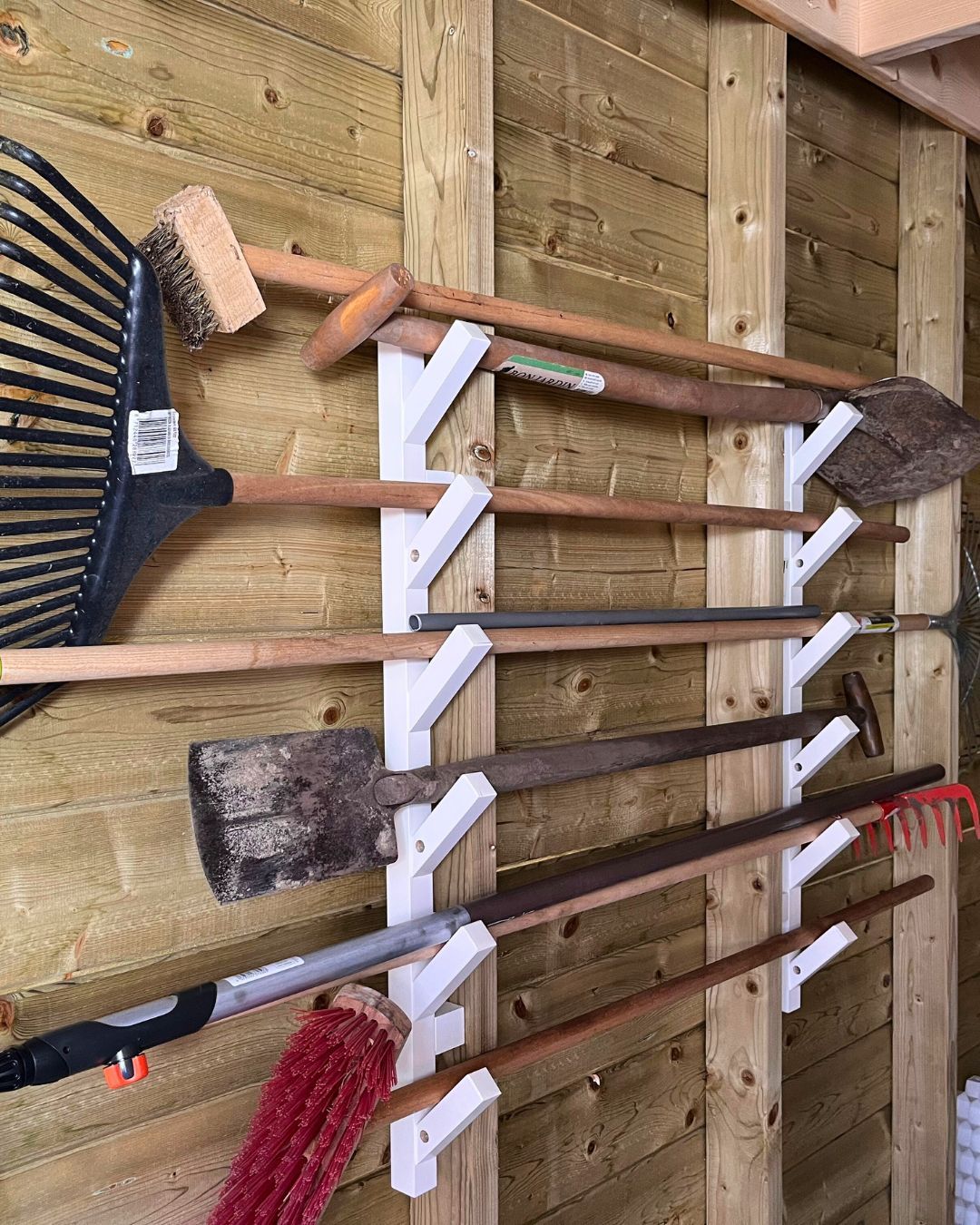 White wall mounted brackets holding long handled garden tools