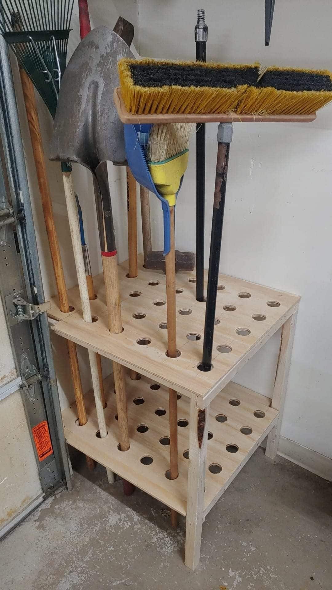 Wood stand with drilled holes holding brooms and tool handles upright