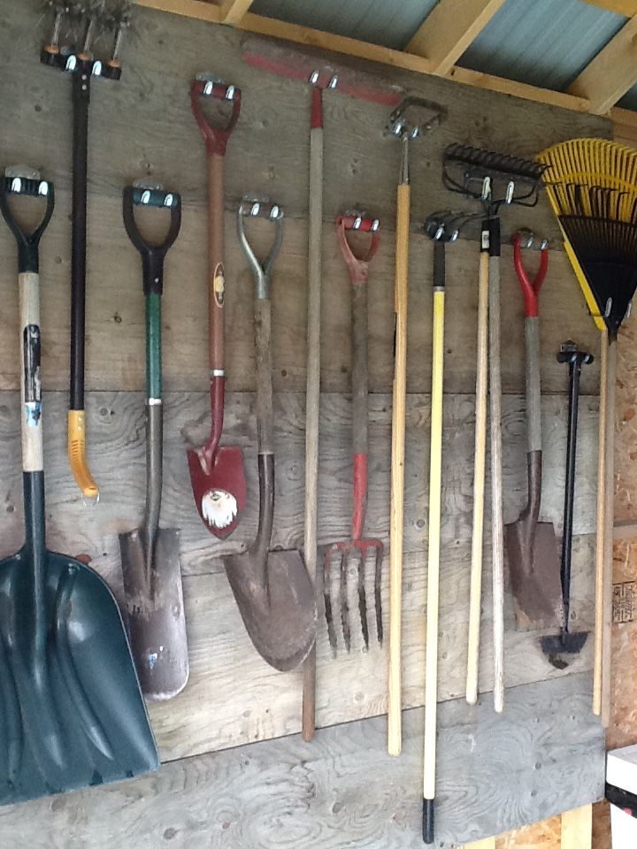Row of wall mounted hooks holding shovels and rakes in a shed