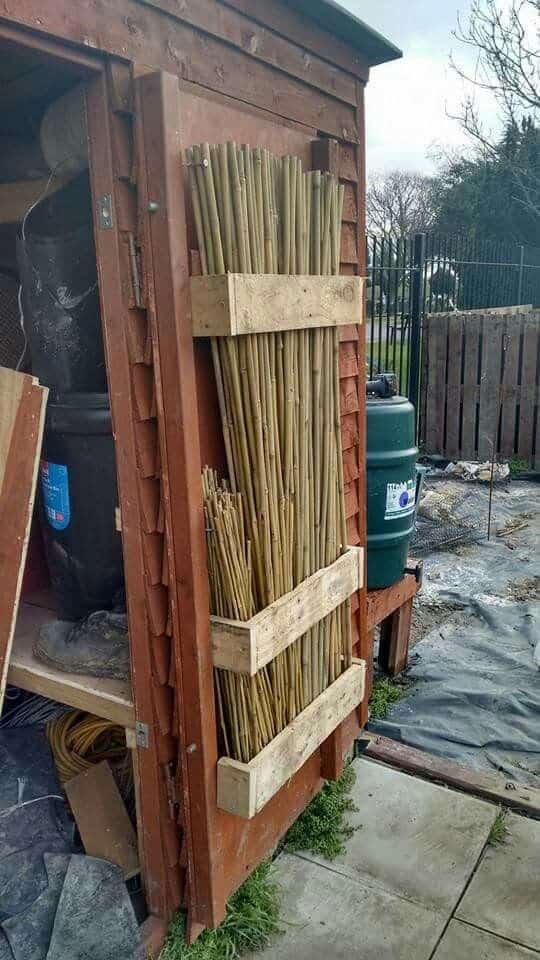 Wood slat rack holding garden canes mounted to a shed door