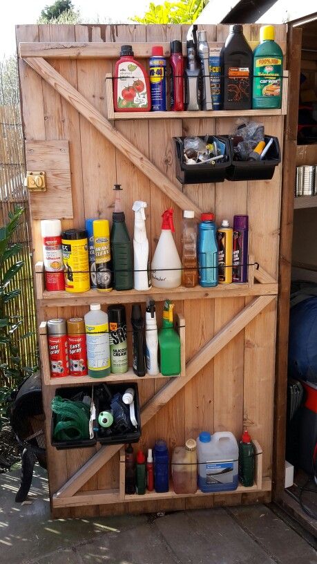 Angled wood shelving on the inside of a shed door holding sprays and bottles