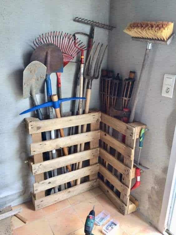 Two pallets stacked in a corner holding shovels, forks, and rakes
