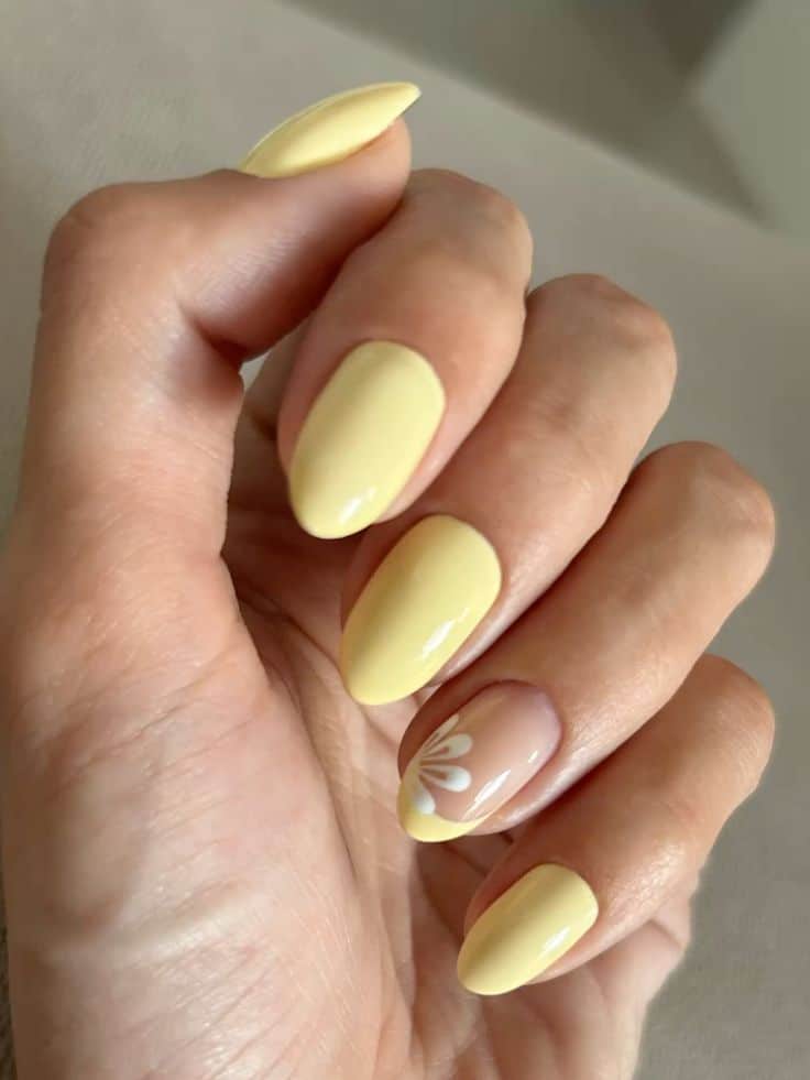 Almond shaped butter yellow nails with a white daisy accent on the ring finger.