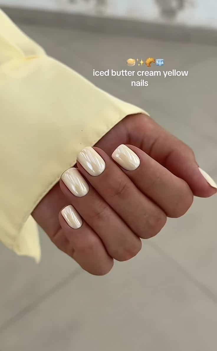 Short square nails in a pearly buttercream yellow with a glossy chrome finish.