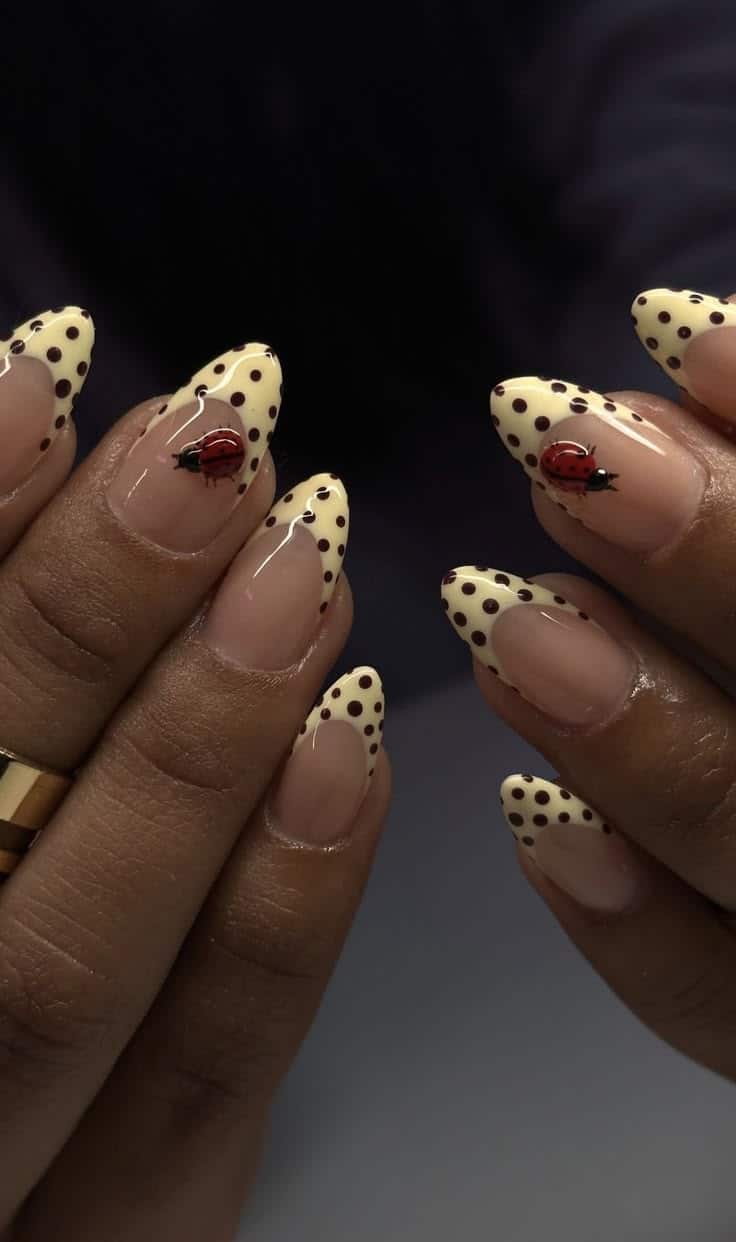 Almond nails with butter yellow polka dot French tips and a red ladybird accent.