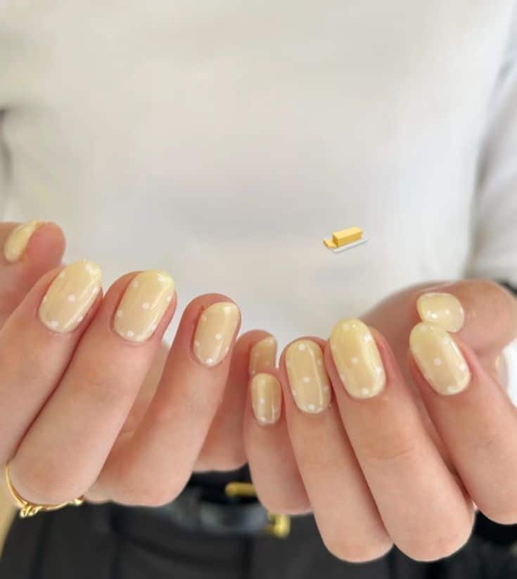 Short rounded nails in a sheer milky butter yellow with small white polka dots.
