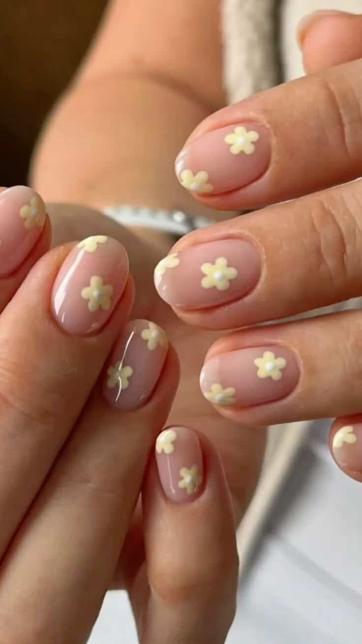 Short natural nails with pale butter yellow flower designs and pearl centres.