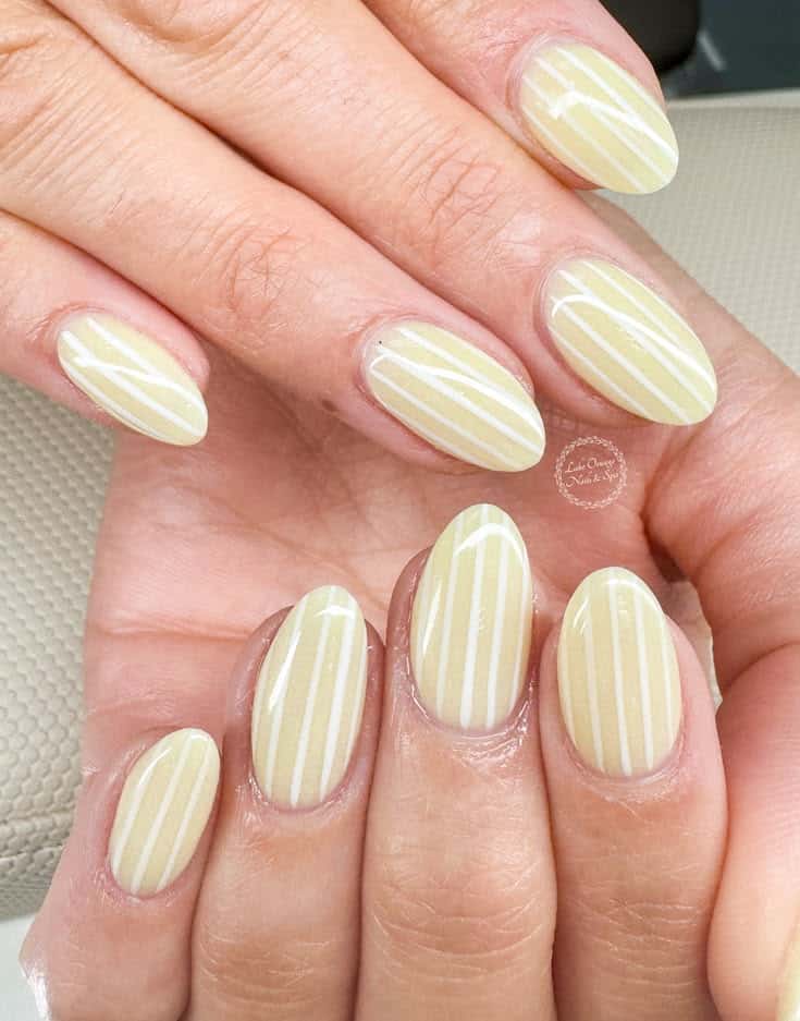 Almond nails in butter yellow with thin vertical white candy stripe details.