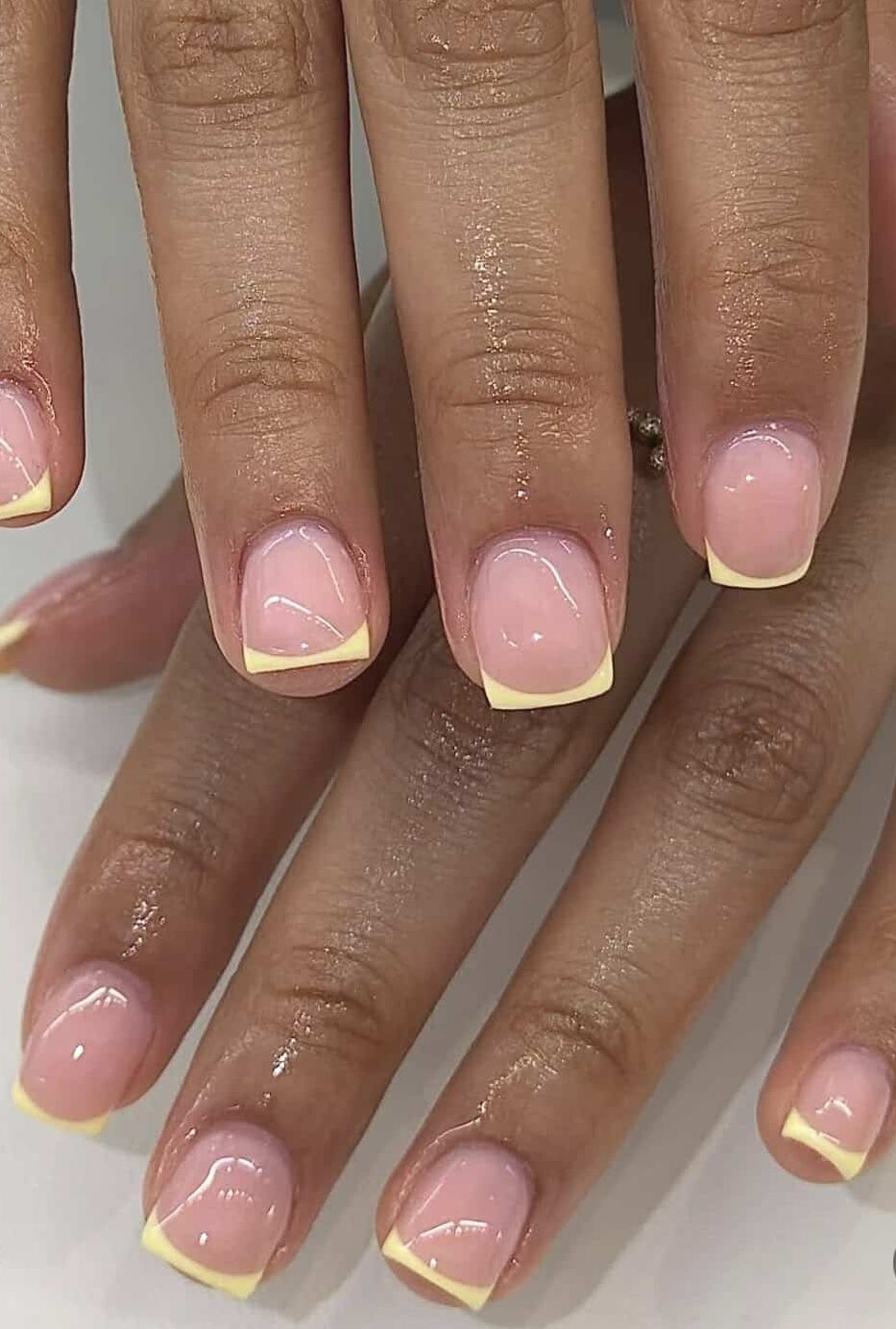 Short square nails with a natural pink base and thin butter yellow French tips